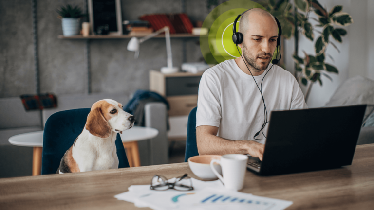 Man wearing a headset and typing on laptop with a beagle dog on the chair next to him